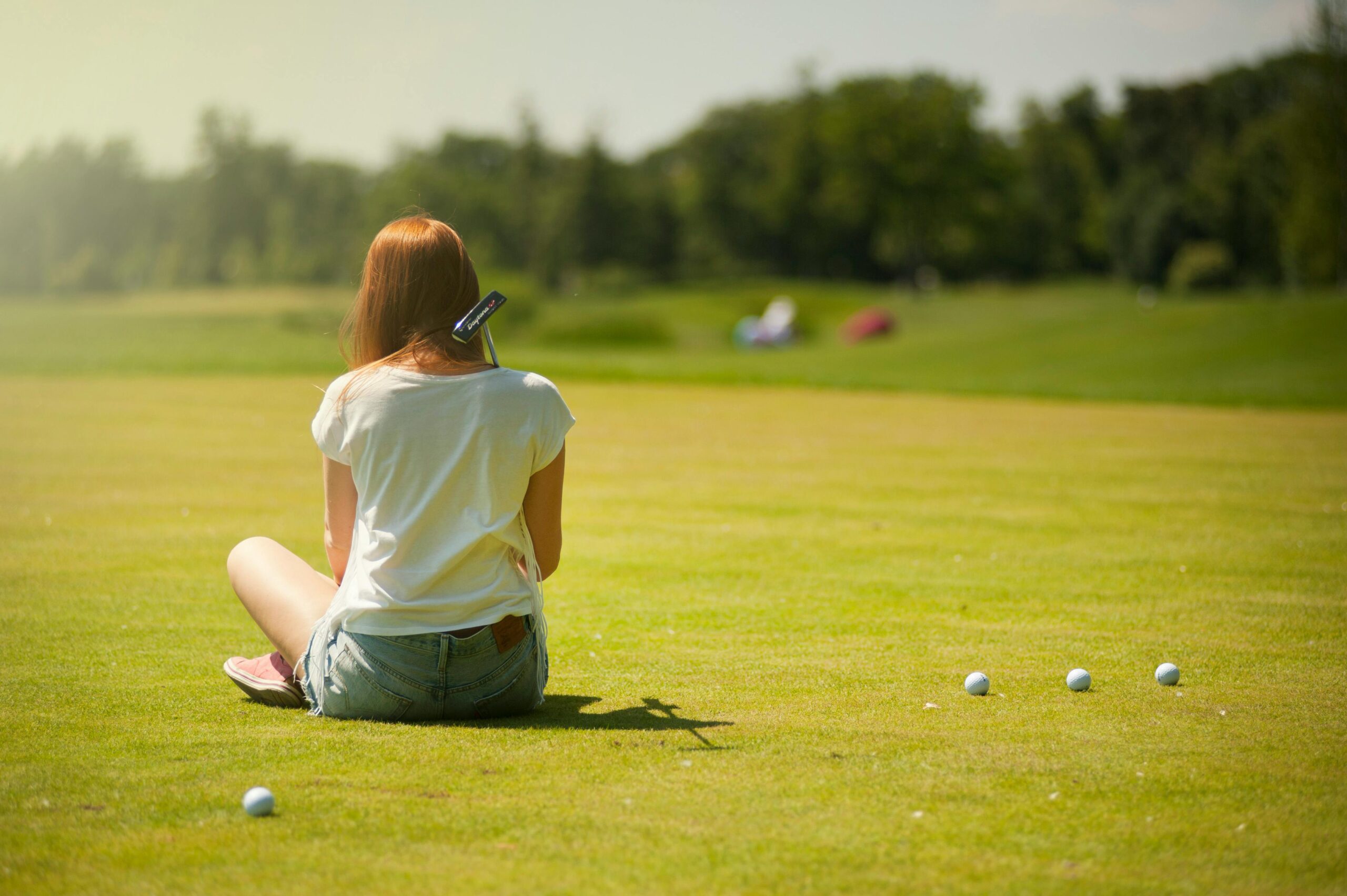 A young woman sitting on a golf course in summer, enjoying leisure time outdoors.